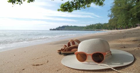 Summer beach with straw hat, sunglasses and flip flops on sandy beach background.