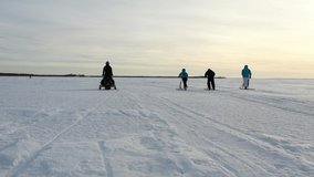 Four persons on the ice doing winter activities filmed. They are riding kicksleds and a snowmobile. The video was shot on the frozen sea in Finland with a drone.