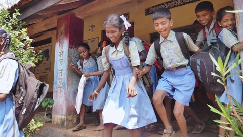 A group of happy cheerful Indian Rural school children wearing uniforms and backpacks leaving or running out of the classroom after the school is over, Kudal, Maharashtra, India (March 2022)