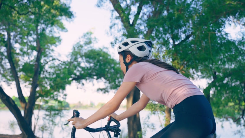 Asian young sport woman riding bicycle in the evening in public park. Beautiful athlete fit and firm girl in sportswear wear helmet, exercise by cycling workout for her health care wellness and fresh.