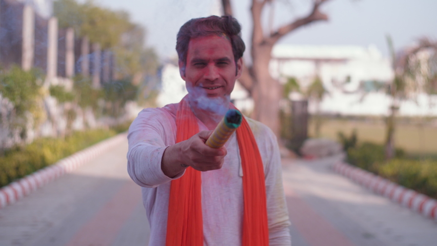 Young Indian man playing with smoke bombs on Holi - environmental hazard, pollution, chemical colors. A handsome guy in ethnic clothes with a dupatta celebrating the spring festival outdoors.