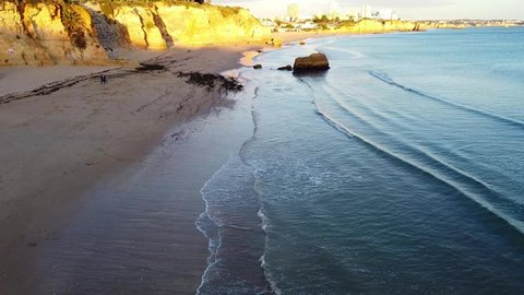 Aerial drone shot over golden Algarve coast looking over beautiful city. Deep blue ocean. City in golden sunset. Pure empty beaches. Sunny day summertime. Aerial view over Algarve coast. Drone footage