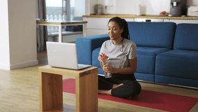 Smiling african american woman talking on video call on laptop while sitting on yoga mat