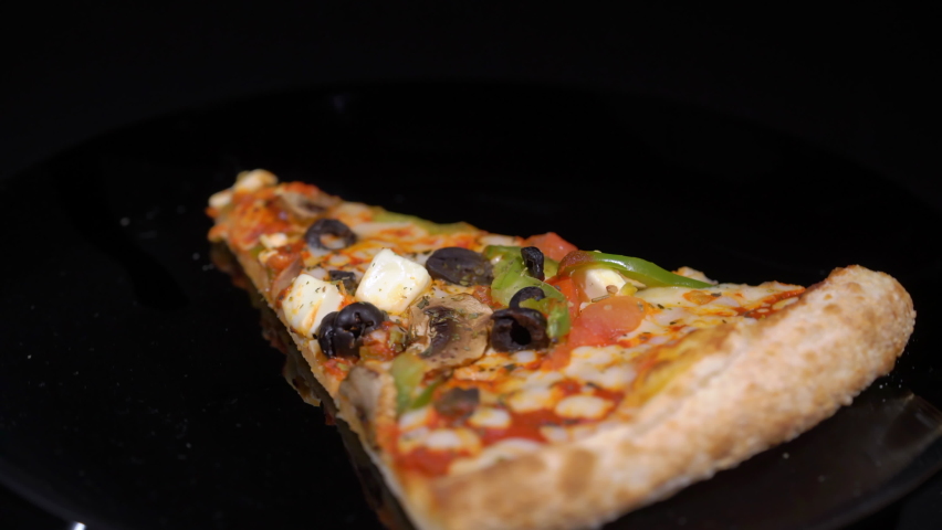 Piece slice of pizza with vegetables and cheese. Olives, pepper and tomato. Food on plate turning on black isolated background. Showcase in restaurant pizzeria.