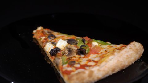 Piece slice of pizza with vegetables and cheese. Olives, pepper and tomato. Food on plate turning on black isolated background. Showcase in restaurant pizzeria.