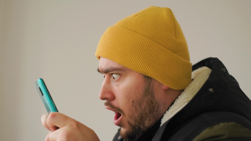 close up of a Crazy and funny face of american bearded man addicted to play mobile game. Angry male holding on the smartphone. Royalty-Free Stock Footage #1087970455