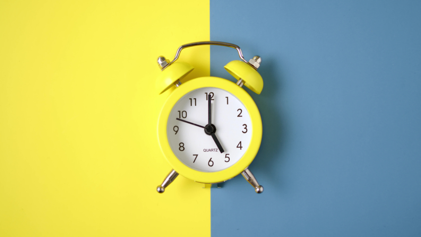 Yellow retro clock lies on yellow and blue background in color of flag of Ukraine divided in half. clock shows 5, time is running out. Five o'clock in the morning, attack time. Royalty-Free Stock Footage #1087971043