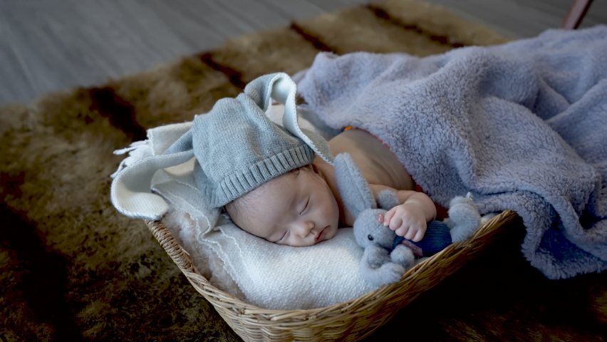 4k, Cute Asian newborn baby. wearing a blue rabbit Sleep well. By hugging the rabbit doll. lying in a wicker basket	