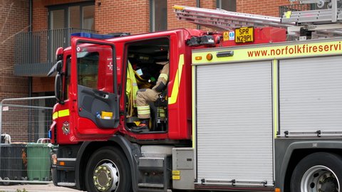 Norwich, Norfolk, United Kingdom. March 4, 2022. Firefighters sit waiting for orders in cab of Scania fire engine with door open and blue lights flashing. 