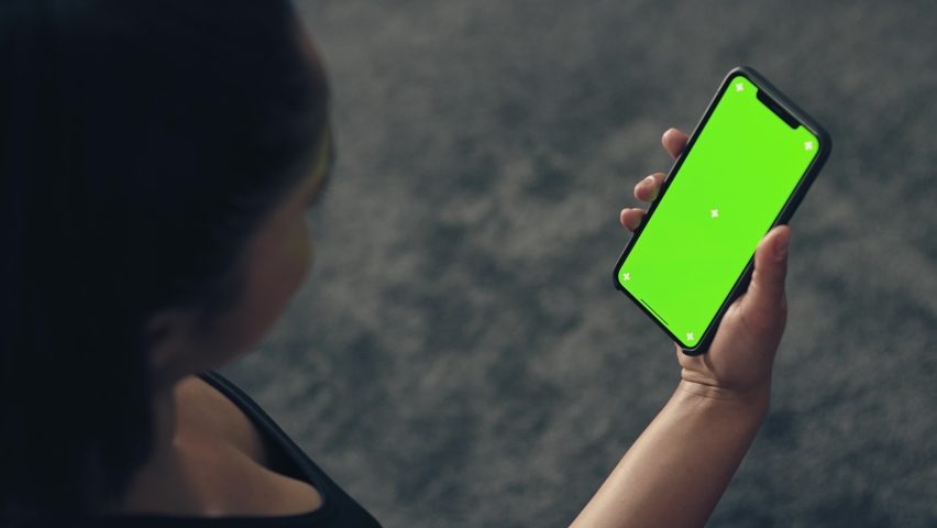 back view of fitness woman using green screen smart phone at home. Woman preparing for workout using smart phone.Woman doing a tap on mobile phone while resting during fitness training Royalty-Free Stock Footage #1087973915
