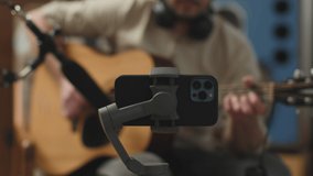 Man playing acoustic guitar, shooting video on phone, using professional mic, blogger recording music. ProRes, closeup