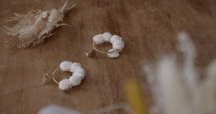 Close up gimbal shot of female hands gluing white flower to earring. High angle