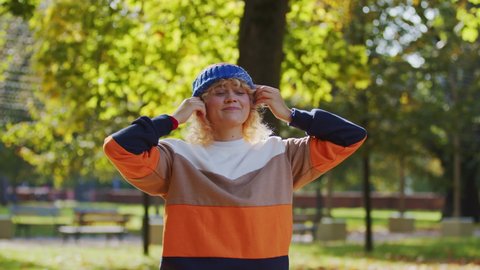 Funny Young Blonde Woman Cover Her Had With Beanie Cap in Park on Sunny Autumn Day, Slow Motion