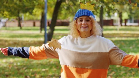 Joyful Young Woman in Sweater and Beanie Running in Park and Throwing Fallen Leaves in Front of Camera, Slow Motion