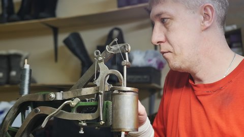 Caucasian male shoemaker adjusts the machine for sewing shoes with a strong thread. Ancient mechanical shoe repair machine