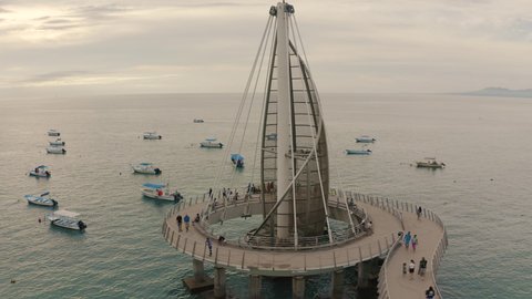 Aerial tour over the iconic The Sail at Pier of Playa los Muertos with many people walking out to sea to watch the beautiful sunset in Puerto Vallarta