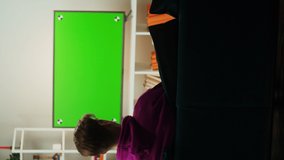 Vertical video of man watching television in living room. Young guy sitting on sofa against tv with green screen, back view. Male person using smartphone with blue chroma key.