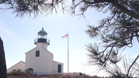 Vintage lighthouse tower, retro light house, old fashioned historic classic white beacon, fresnel lens, american flag. Nautical navigation, coastal building 1855. Point Loma, San Diego, California USA