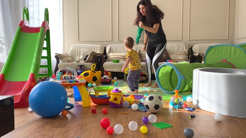 Mom and two children are dancing in the children's room among the scattered toys. A mess in the children's room. Children among scattered toys