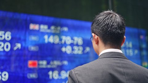 Depressed businessman in front of an electric bulletin board. Japanese translation: "yen","dollar","euro","pound"