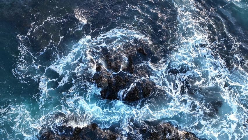 Colorful waters of the ocean, swirl around the rocky and scenic coastline. Sea waves breaking over rocks. | Shutterstock HD Video #1087990867