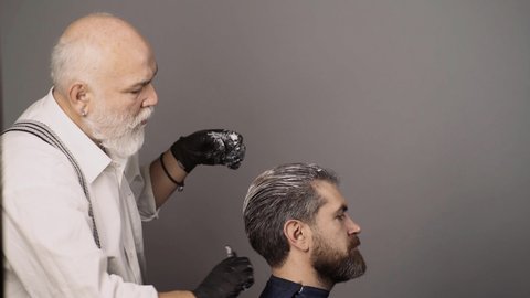 Coloring man hair process. Dyed hair for a bearded hipster guy. Hairdresser applying dye to man hair.