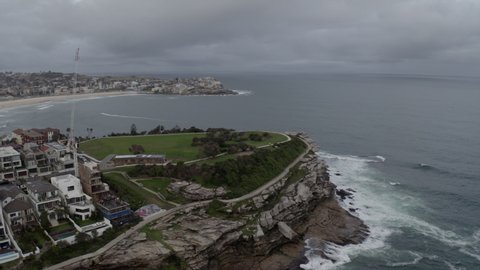 Aerial: Drone flying over the peninsula towards Bondi Beach on a dark, wet, grey and stormy day, in Sydney Australia
