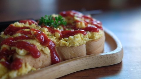 Panning shot of scrambled eggs on toasted bread with ketchup, breakfast in morning at home.