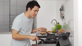young man cooking and preparing food according to a recipe on a tablet computer in the kitchen at home