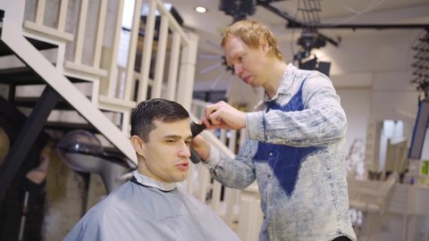 the hairdresser makes a haircut for a brunette man with a hair clipper in a barbershop. professional services. beauty salon for men. cosmetics and products for scalp and hair care.