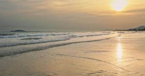 White foam of rolling waves in Sanya, Hainan Island, China. Beautiful seascape. Yellow sand beach, azure sea and beautiful sky clouds at sunset.