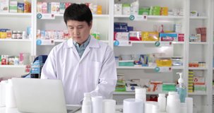Asian pharmacist male looking laptop computer checking medication details and talk about with female pharmacist in pharmacy drugstore, 4k video 