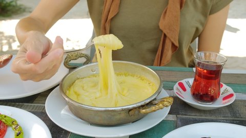 Muhlama or Kuymak dish is a corn flour with cheese traditional dish of a Turkish cuisine. Unidentified woman winding on a wooden spoon Kuymak dish. Glass of turkish tea on the table