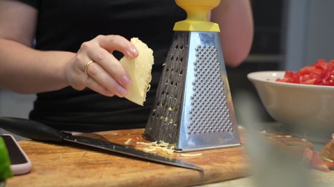 Woman rubs cheese on grater at home in kitchen. closeup female Hand rubs hard cheese on a metal grater. Cheese crumbles smoothly on a cutting board.