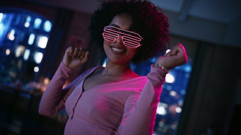 Close Up Portrait of Multiethnic Young Black Female Dancing in Futuristic Neon Glowing Glasses, Having a Party at Home in Loft Apartment. Recording Funny Viral Videos for Social Media. Slow Motion.