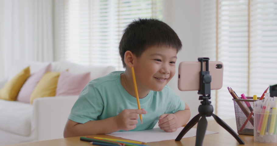 Asia cute smart boy alpha gen z kid enjoy fun hobby idea paint pencil color game on paper at online day care play school by vlog talk video call app. Young son study class tutor teach at home table. Royalty-Free Stock Footage #1088006541