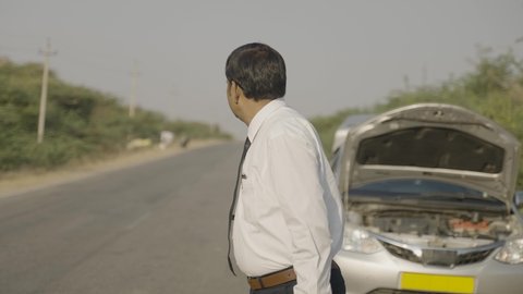 Businessman asking for lift or hitch hiking on road due to car breakdown - concept of asking help, trouble and transportation.