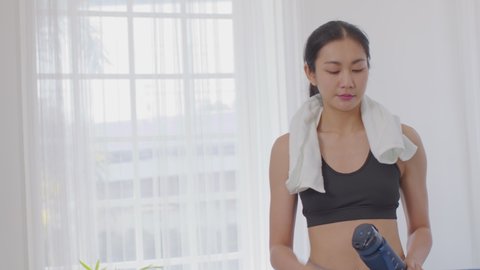 Athletic Healthy Asian young woman in sportswear drinking water after workout exercise at home.Young sporty female take a break and drinking protein shake resting and relax.healthy lifestyle concept