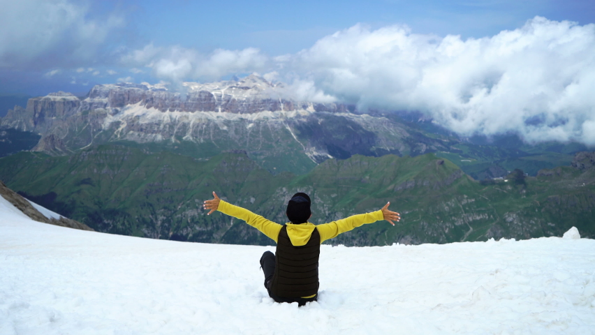 Woman sitting on mountain peak with arms outstretched, Italy, glacier Marmolada 
