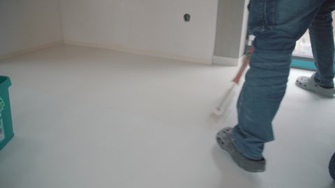 Construction worker performs floor screed indoors. Self-priming freshly prepared floor. 4K