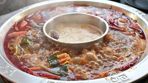 Footage of Boiling spicy Chinese hotpot. Hotpot is an interactive meal in which diners sit around a simmering pot of soup at the center of the table with ingredients.