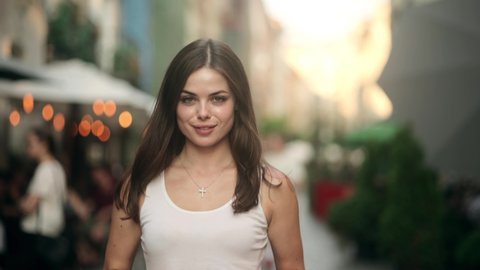 Happy young beautiful woman walking on the street. Portrait of cheerful girl looking at camera. Portrait of a Gorgeous Dark Haired Woman Smiling Charmingly