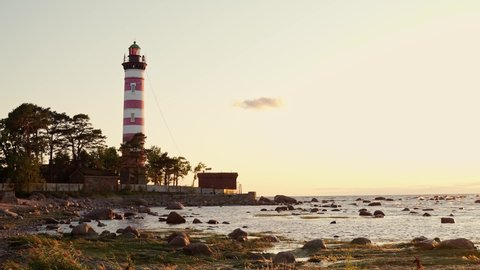 red-white lighthouse on a rocky shore in the warm rays of the sunset