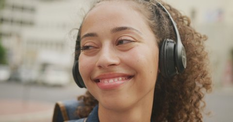 Happy biracial woman in city, wearing headphones and smiling. digital nomad on the go, out and about in the city.
