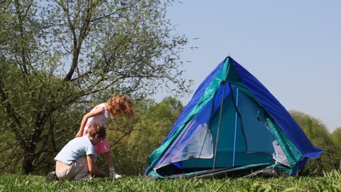 boy and little girl pull cords of tent in woods hot summer