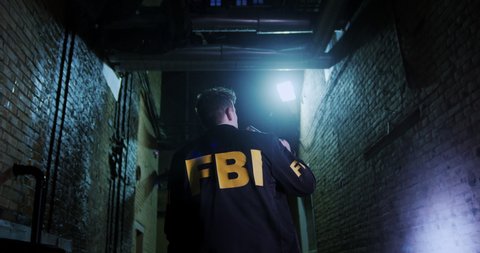 An FBI agent in a jacket conducts an investigation at night on a city street. Lighting the road and the street with a flashlight, the special agent examines the crime scene.