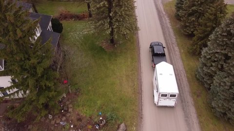 Black pick up truck towing horse trailer through small town, aerial follow view