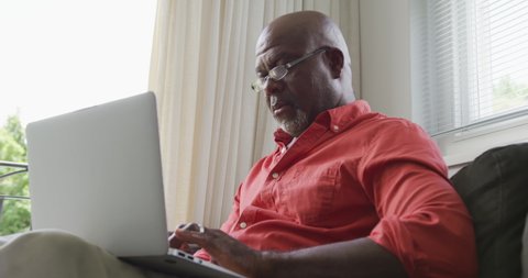Senior african american man sitting and using laptop in living room. spending time alone at home.