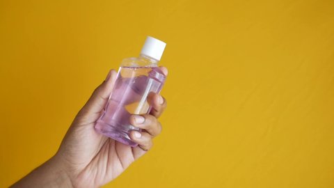  hand hold a mouthwash liquid container on yellow background 