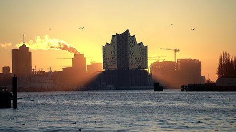 Sunrise behind the Elbphilharmonie, a small ship is travelling and a moll is flying